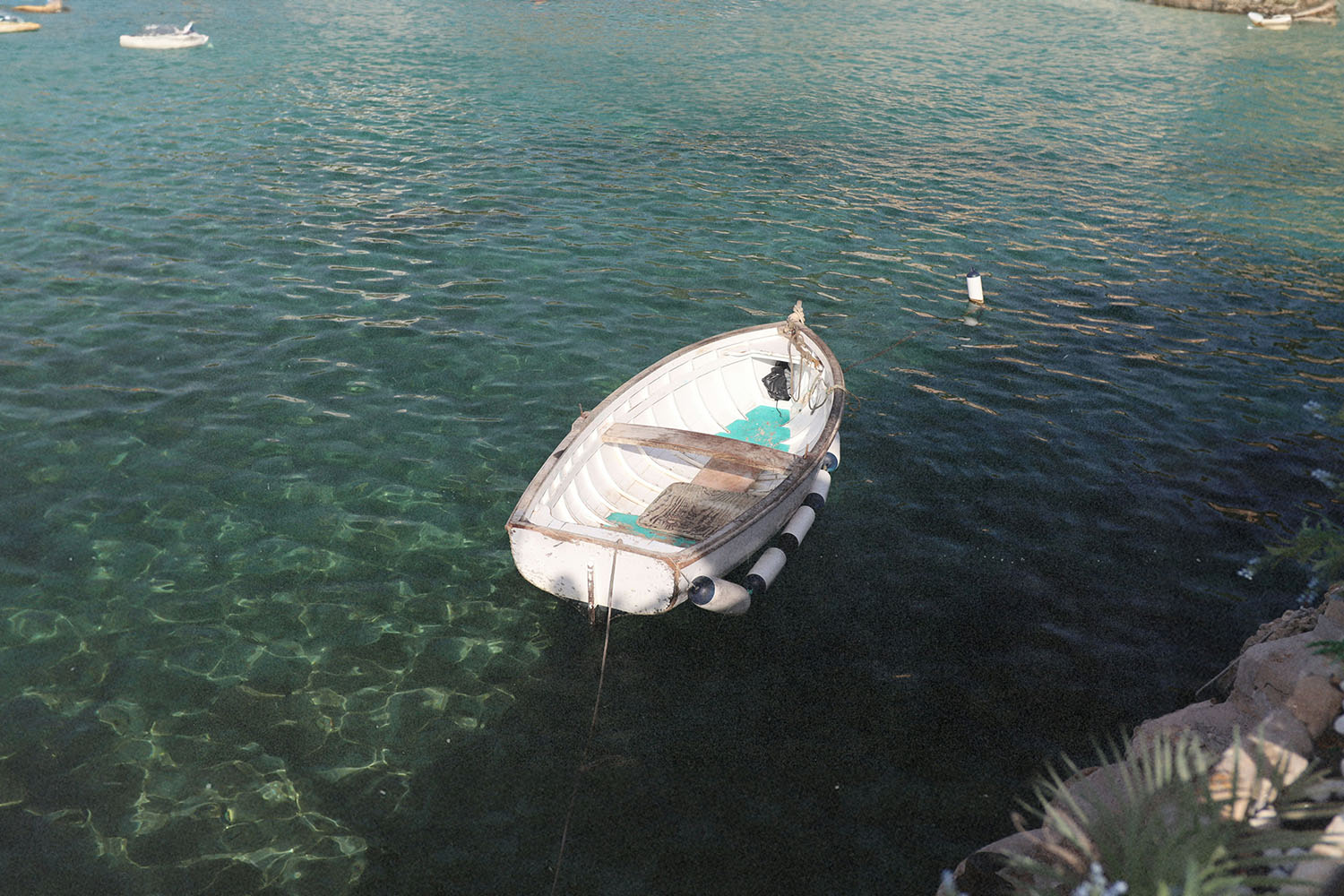 A small white rowboat floats gently on clear turquoise water near a rocky shoreline