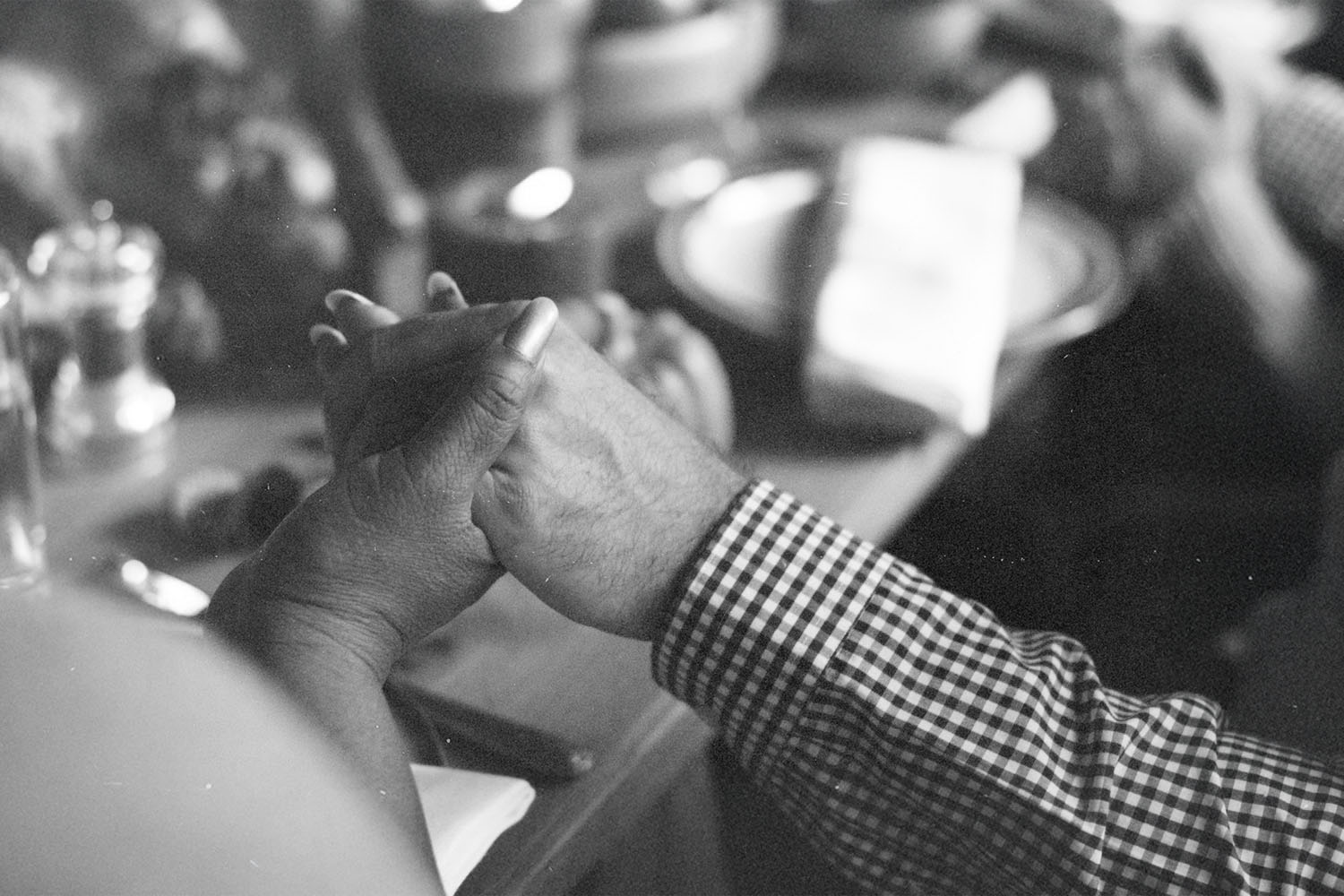 Two people hold hands across a table set with plates, bowls, and candles in a warm, intimate setting