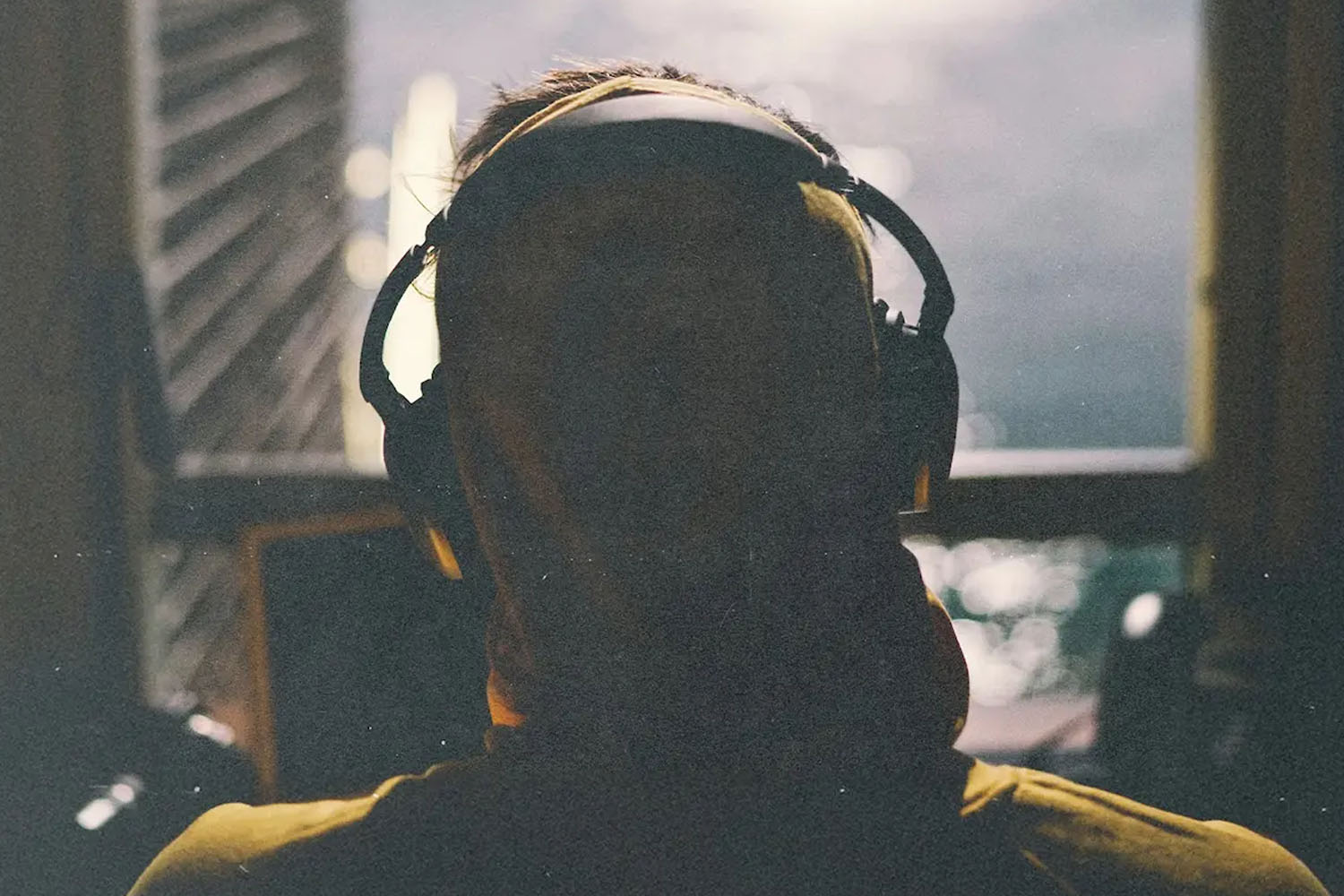 A person wearing large headphones is silhouetted against soft window light, with the background slightly out of focus