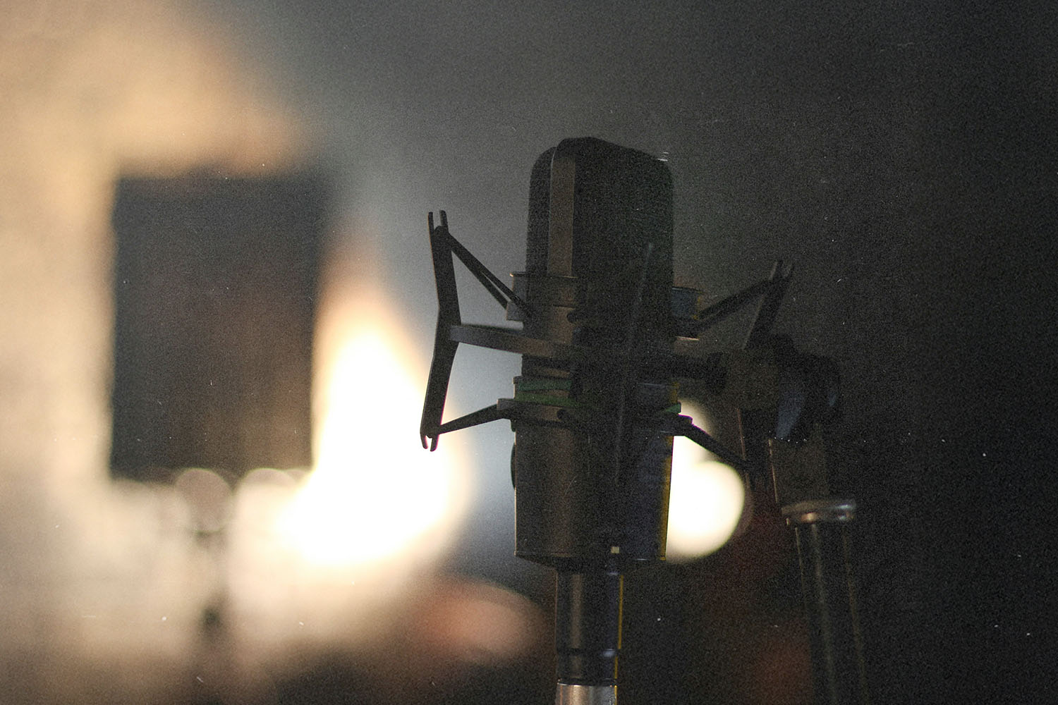 A close‑up of a studio microphone on a stand, lit from behind by a warm, blurred light source