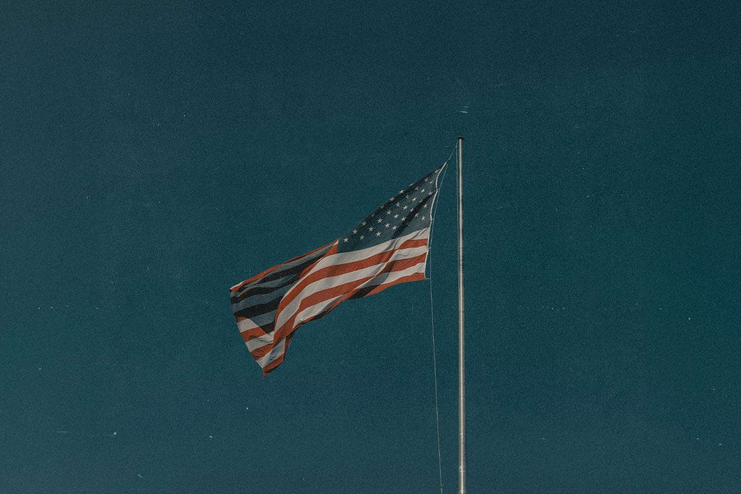 An American flag waving on a tall flagpole against a deep blue sky