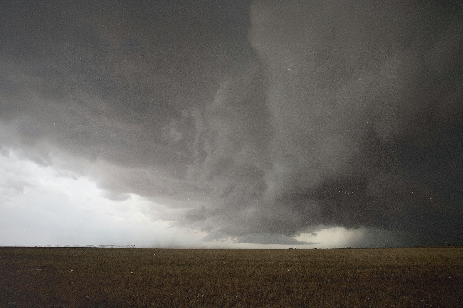 Massive storm cloud spreads dramatically across the sky above a flat, open field