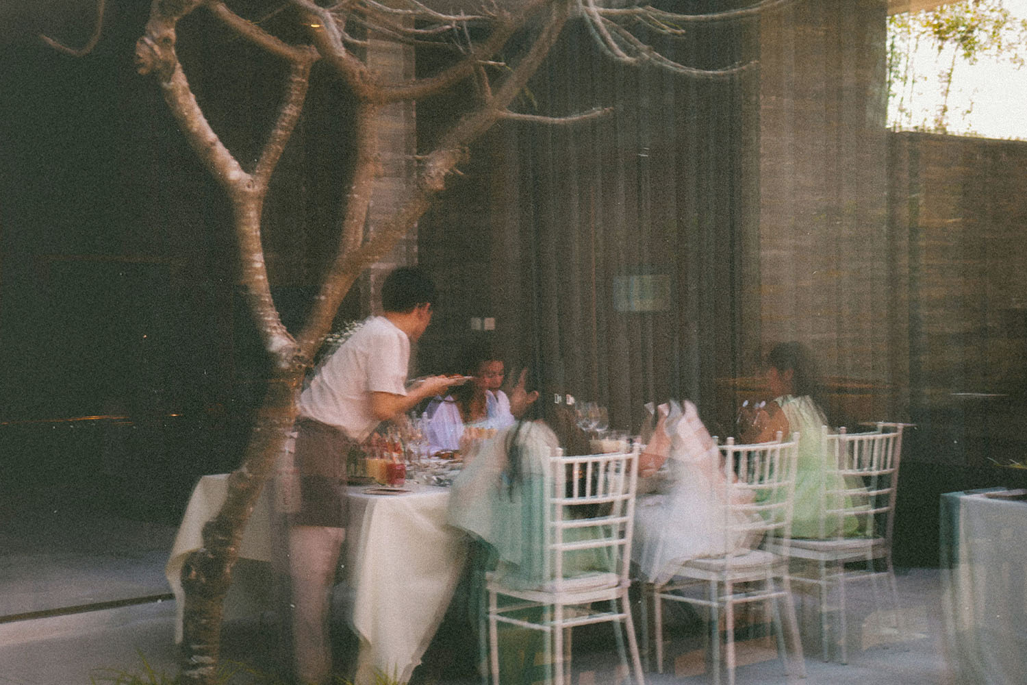 Server attending to a group of people dining at an outdoor restaurant, seen through a glass window with soft motion blur