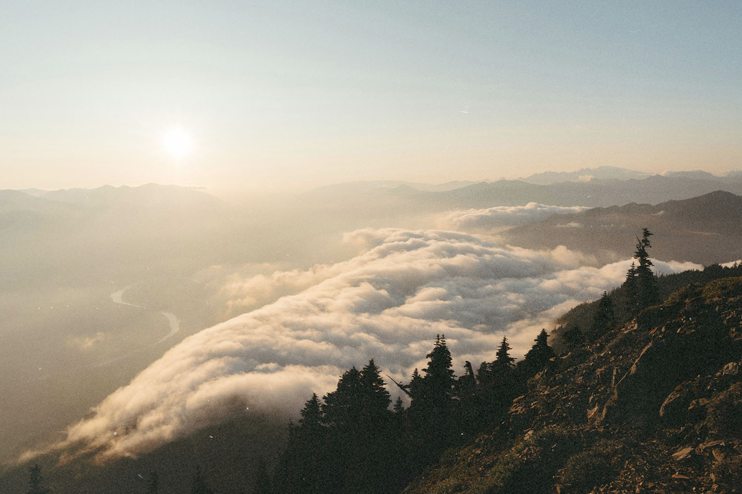 Sunrise casting warm light over mountain ridges and a valley filled with rolling clouds