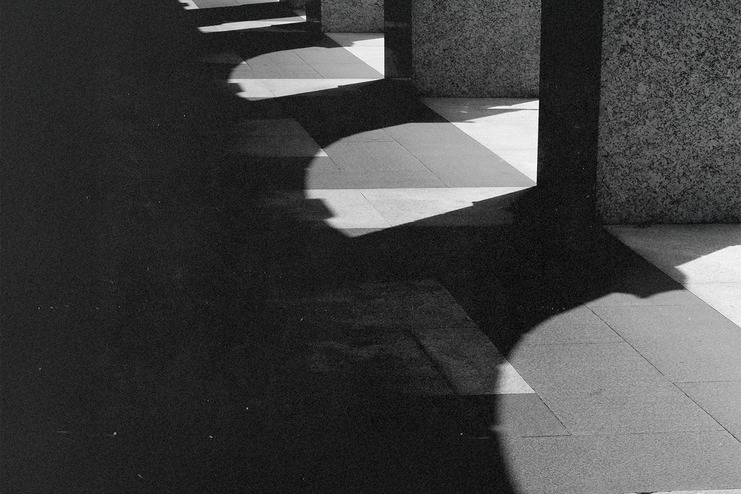 Strong contrast of light and shadow cast by a row of stone columns onto a tiled walkway