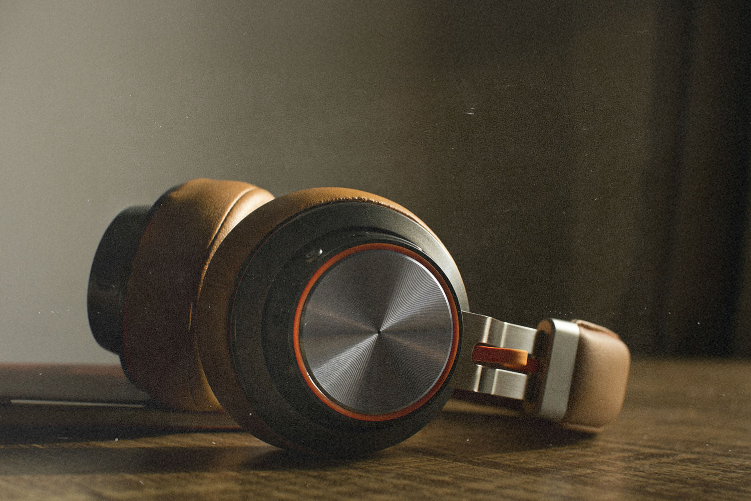 Close-up of brown over‑ear headphones resting on a wooden surface in soft, warm light