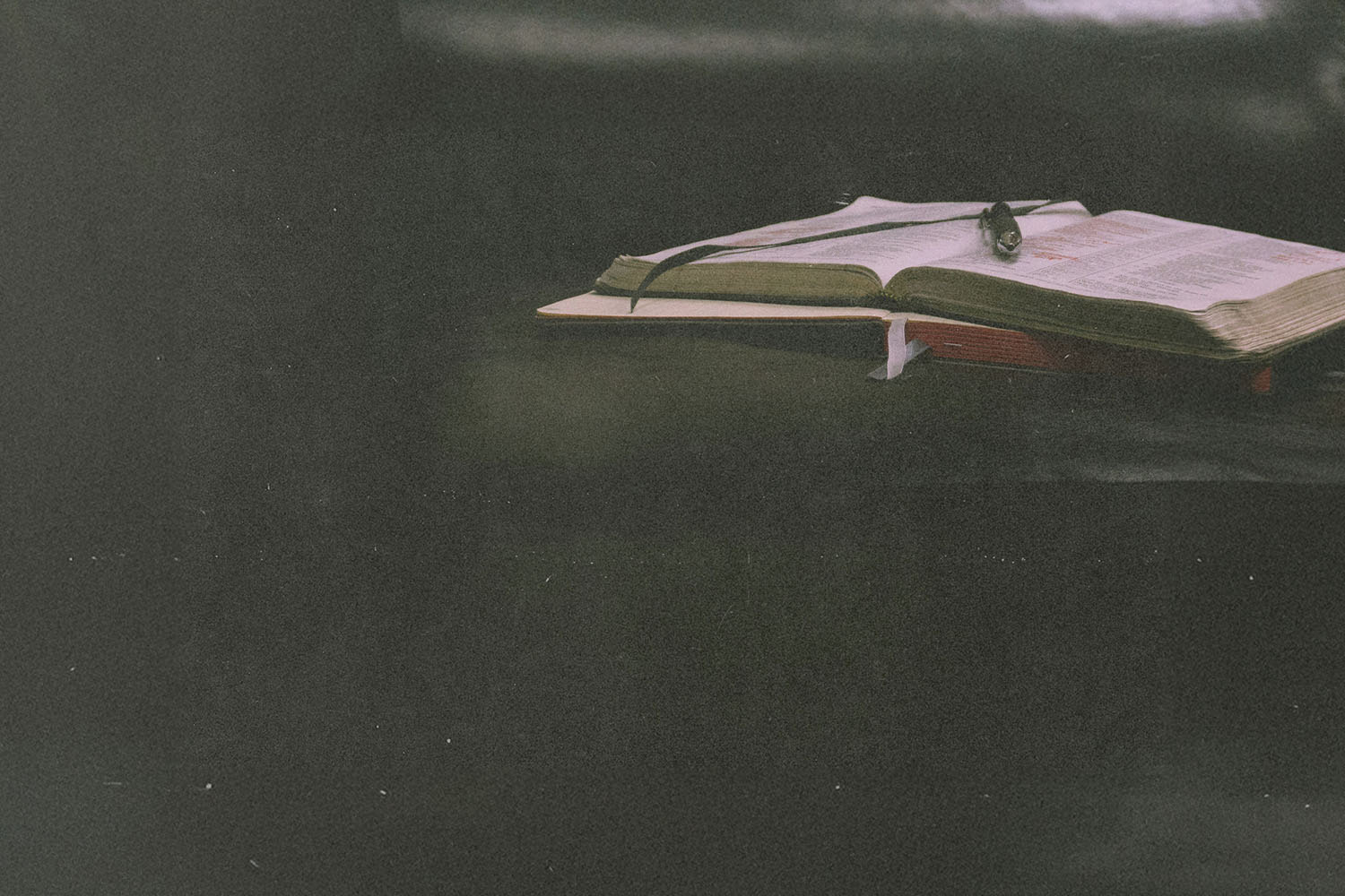 Close-up of an open Bible with a ribbon marker and reading glasses placed on top, set against a dark background