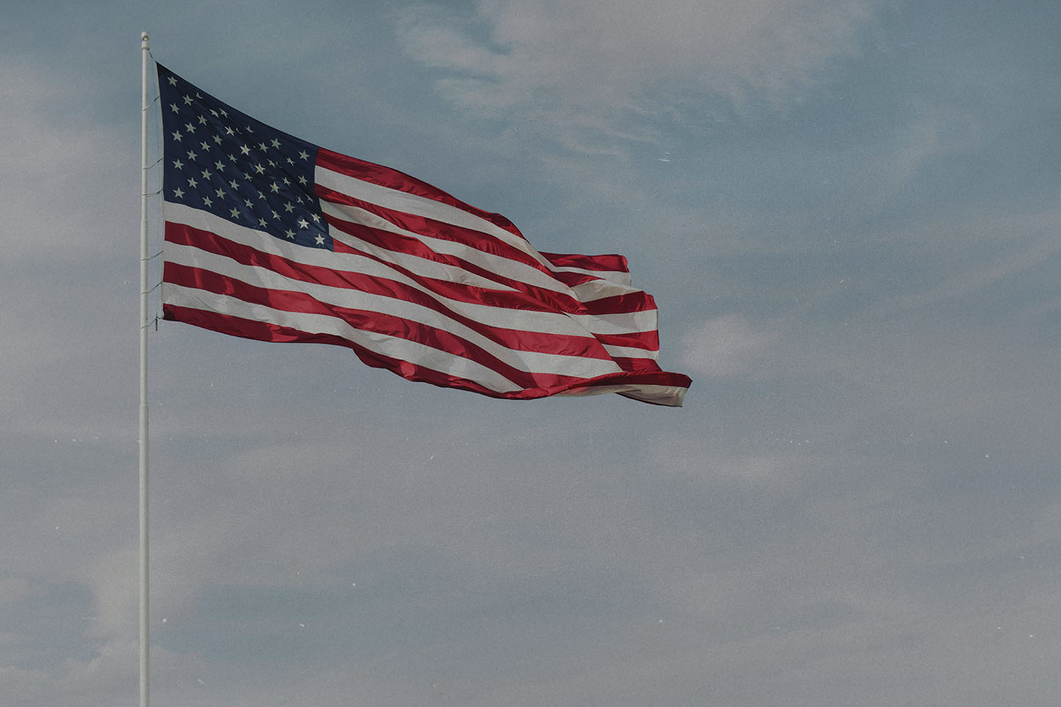 American flag waving on a tall flagpole against a partly cloudy blue sky