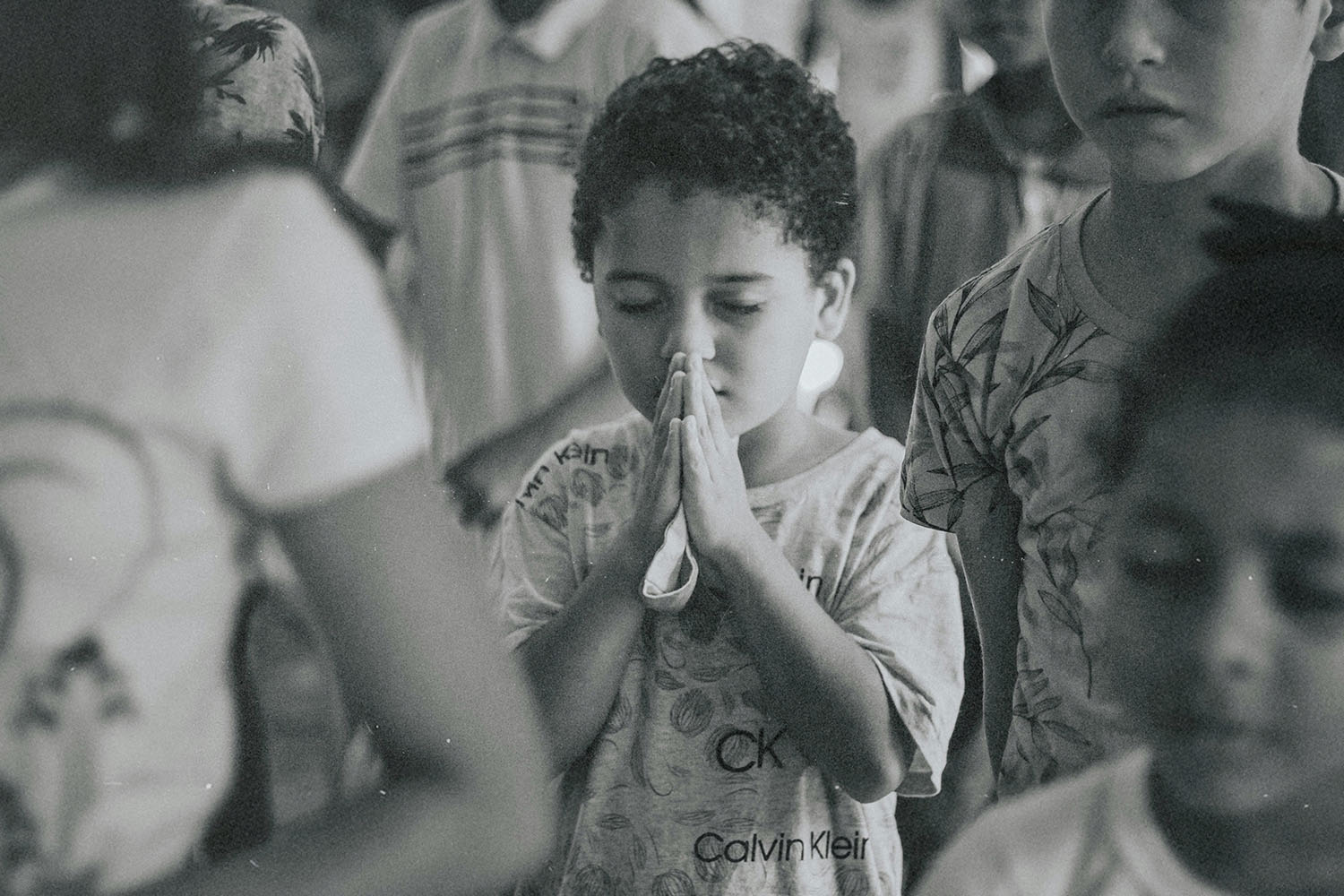 hild standing in a crowded room with hands held together in a prayer posture