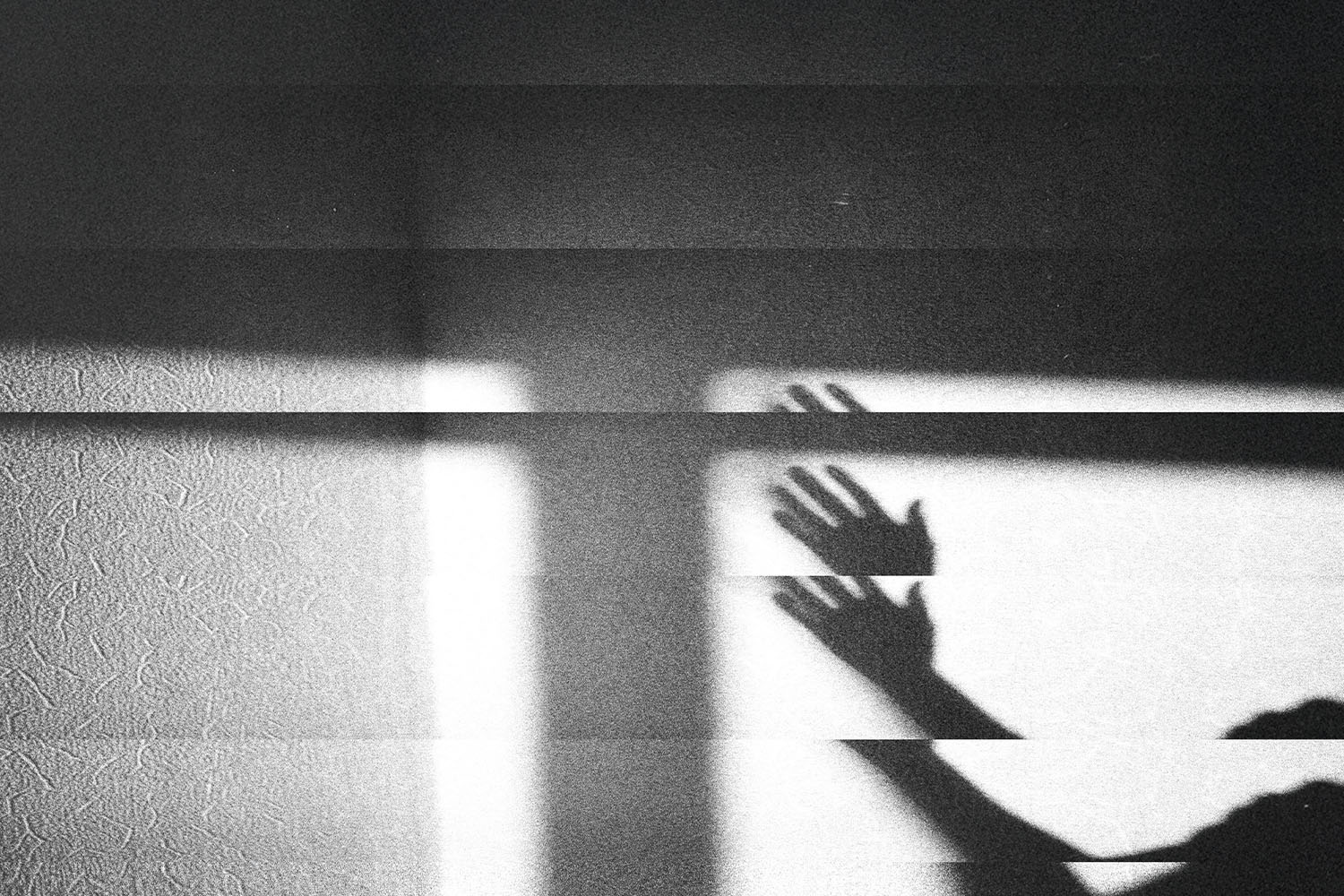Shadow of raised hands cast across a textured wall in dramatic light and dark bands