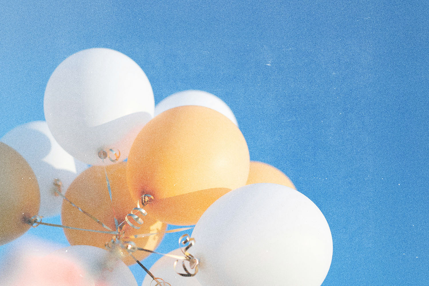 White and golden balloons rising toward a cloudless blue sky