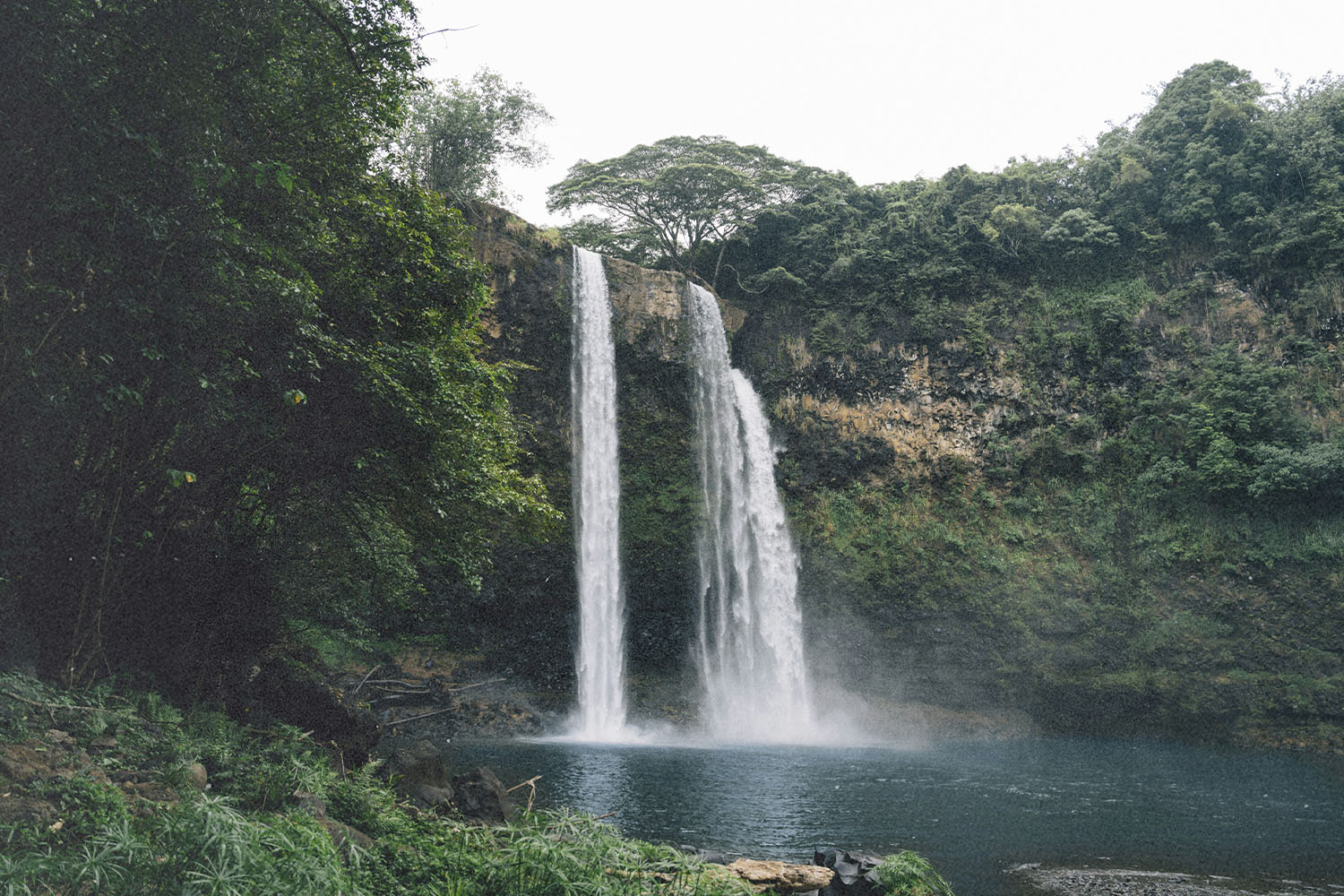 Twin streams of water falling from a green, moss-covered cliff into a misty basin