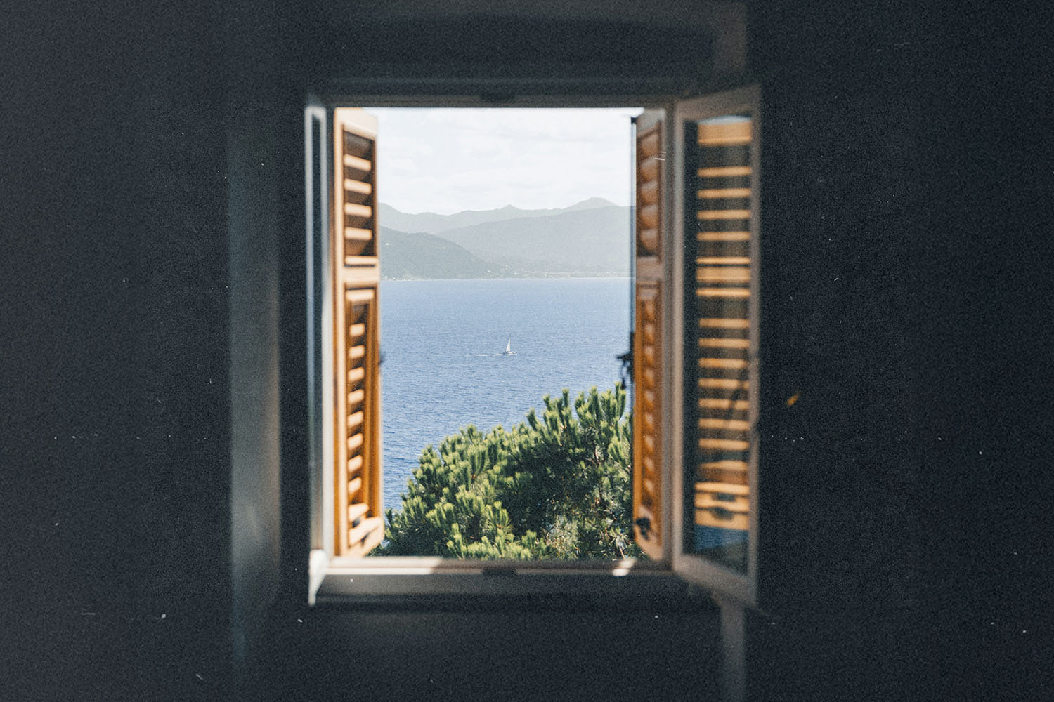 unlit seascape framed by an open window overlooking blue water and rolling hills
