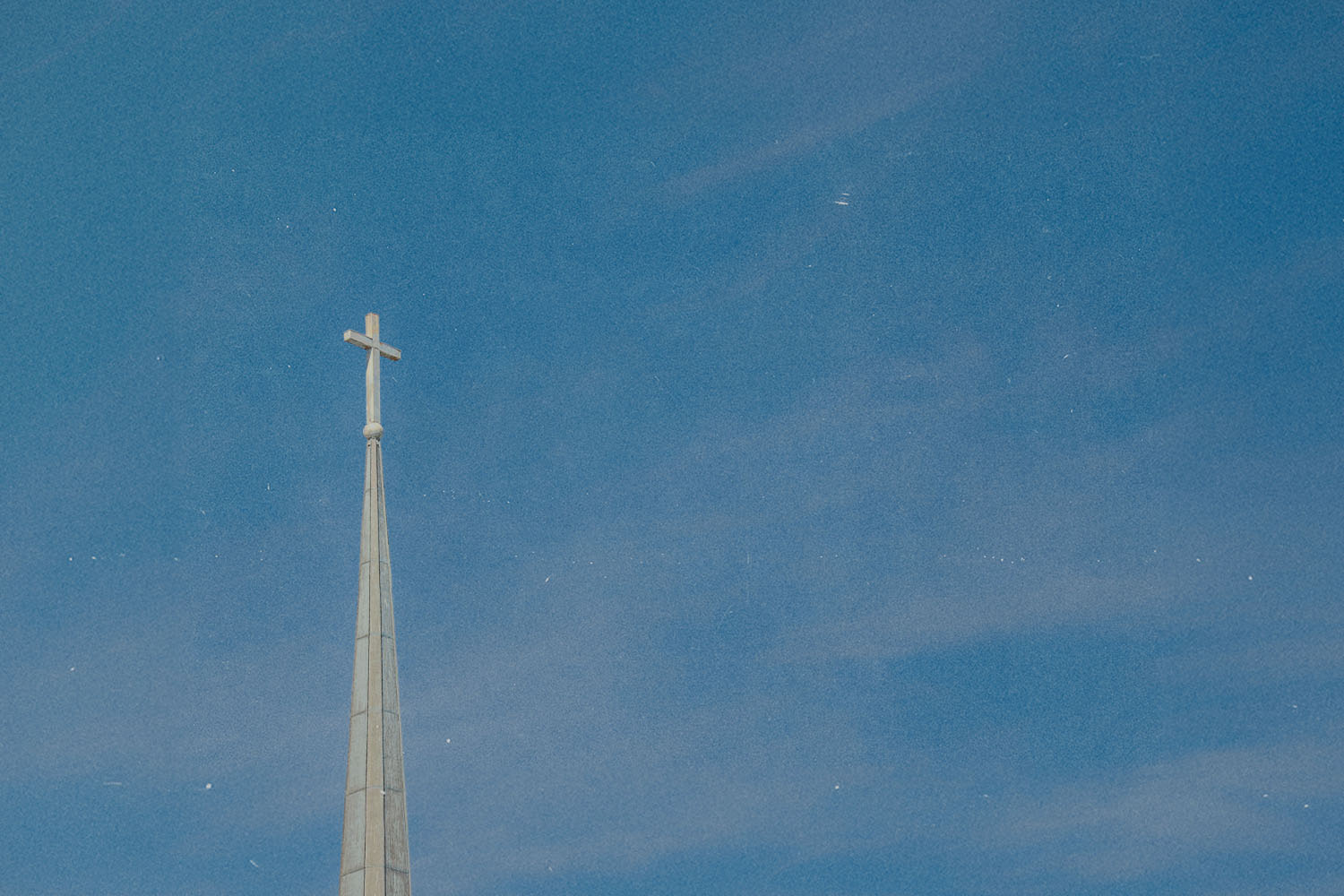 A church steeple with a cross at the top rises into a clear blue sky