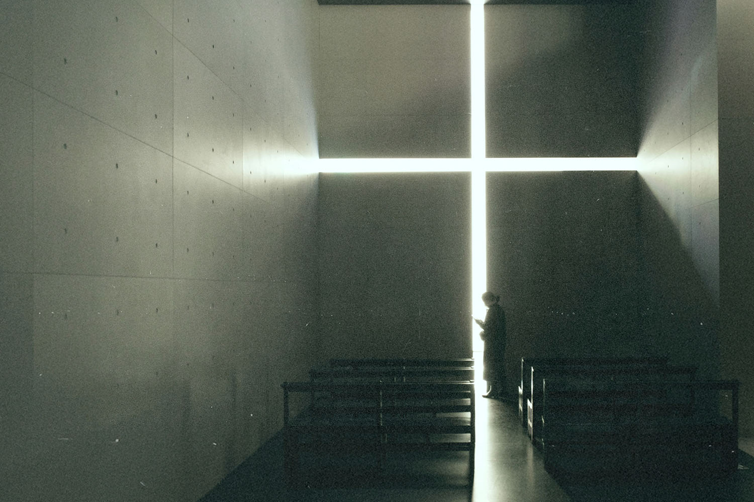 A person stands inside a dimly lit chapel, silhouetted against a large glowing cross-shaped opening on the far wall