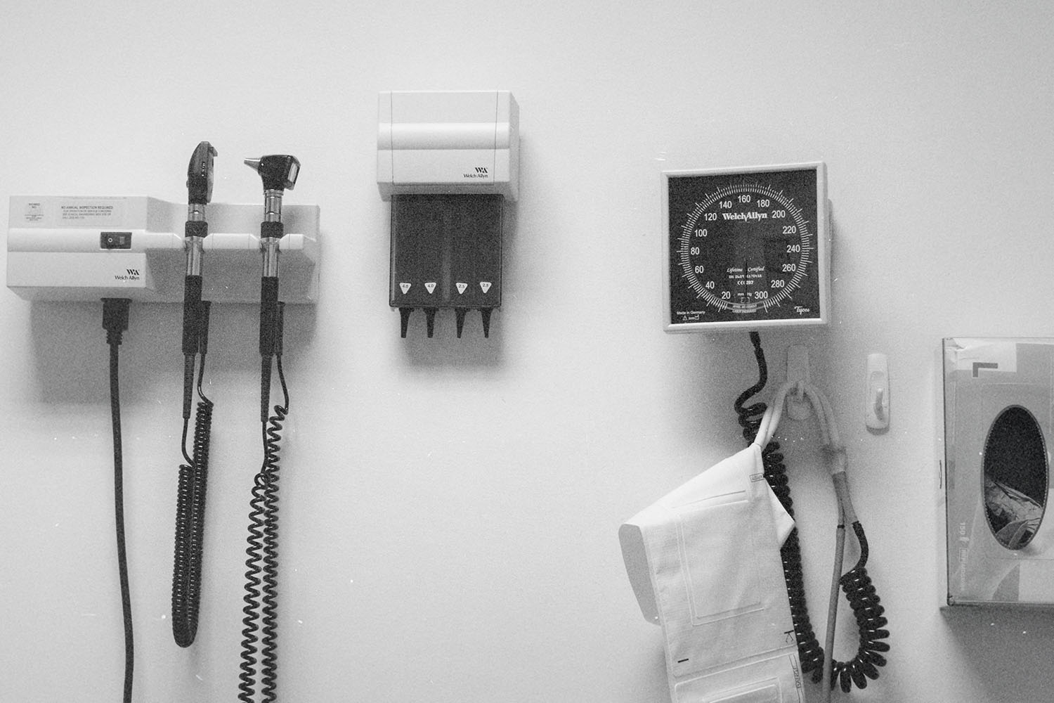 Wall-mounted medical equipment, including an otoscope, blood pressure gauge, and storage units, arranged neatly in a clinical exam room
