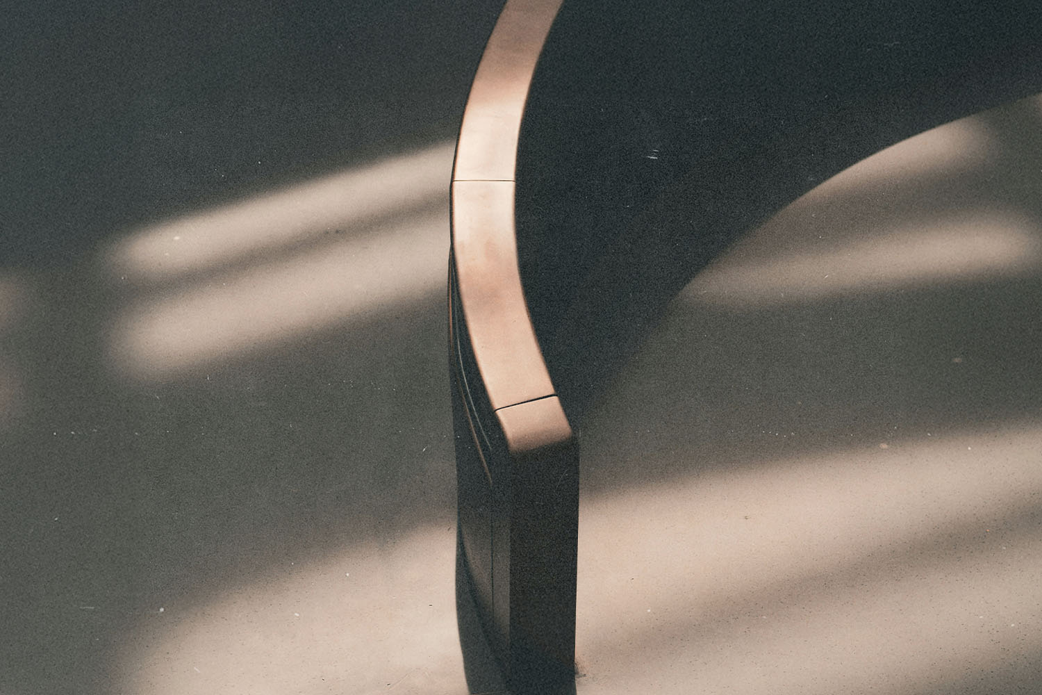 A curved wooden bench sits in soft, slanted sunlight, casting smooth shadows across the floor