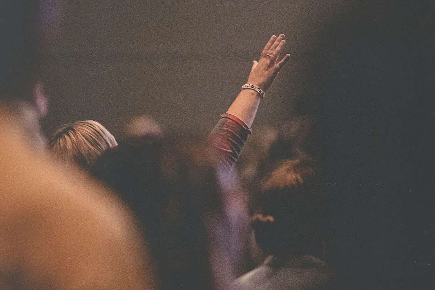 Individual lifting an arm in a crowded indoor space, surrounded by blurred crowd