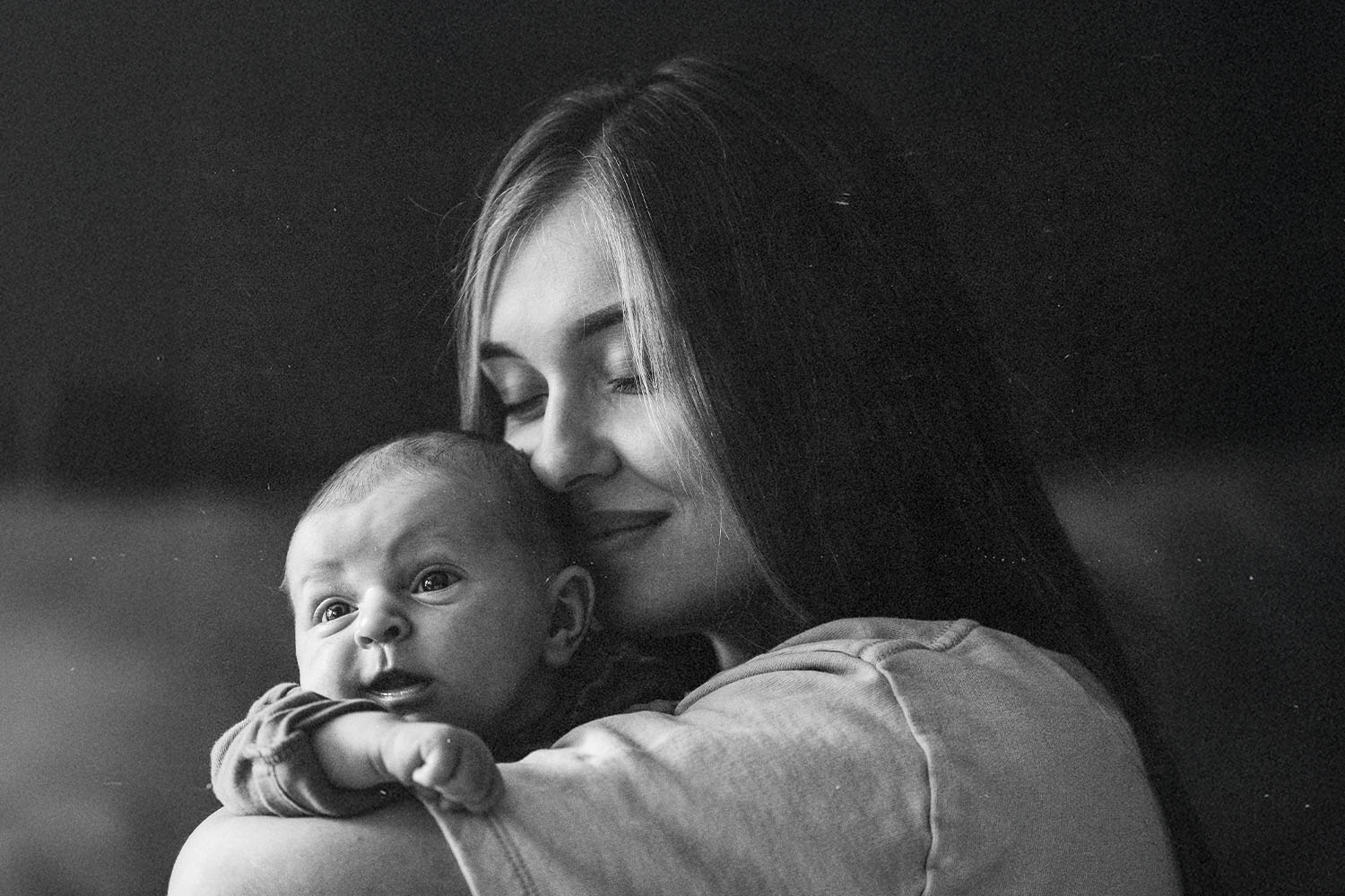 Woman holds a small baby close against her shoulder in a quiet, softly lit setting