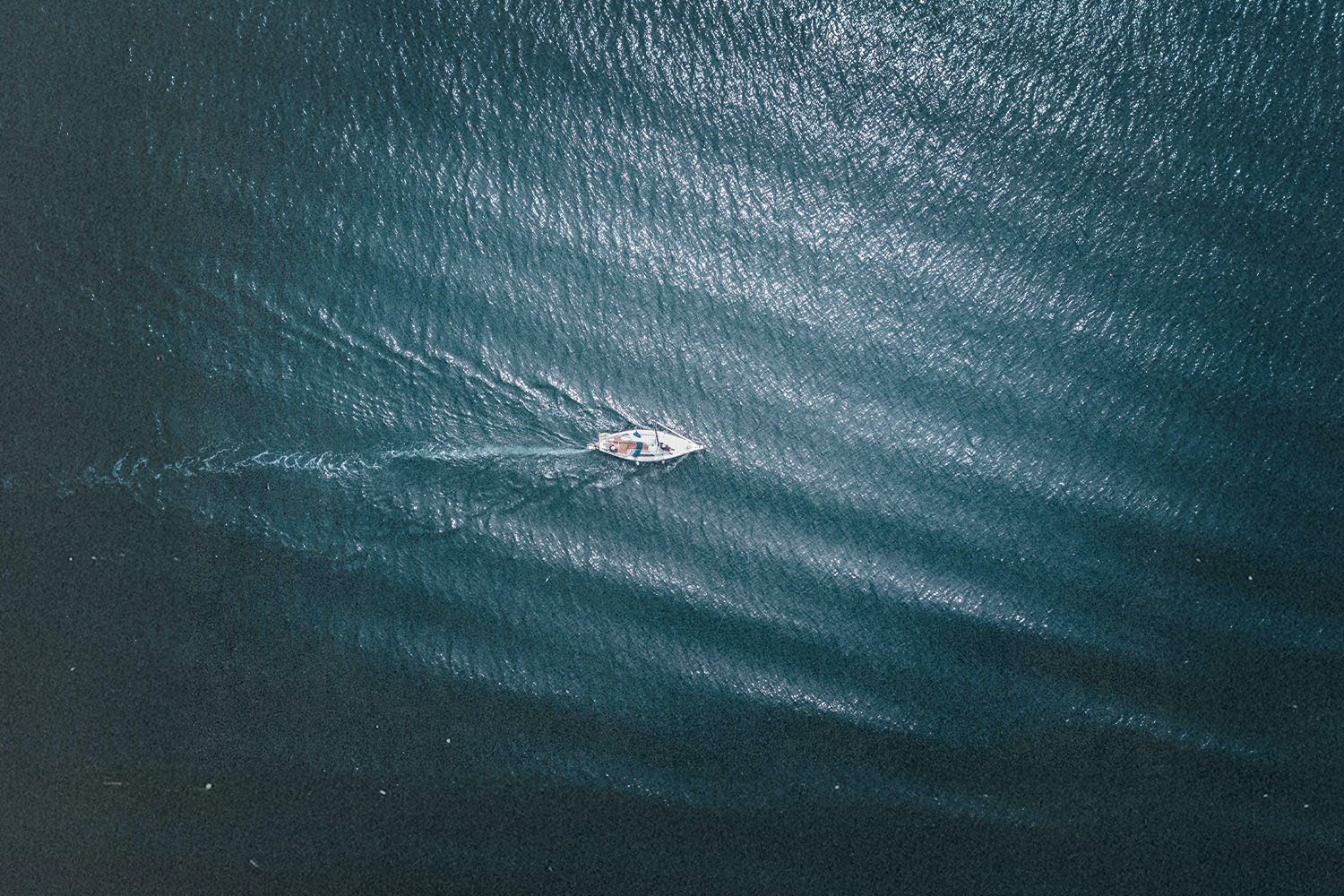 “Aerial view of a small boat moving across deep blue water, leaving a soft wake behind it
