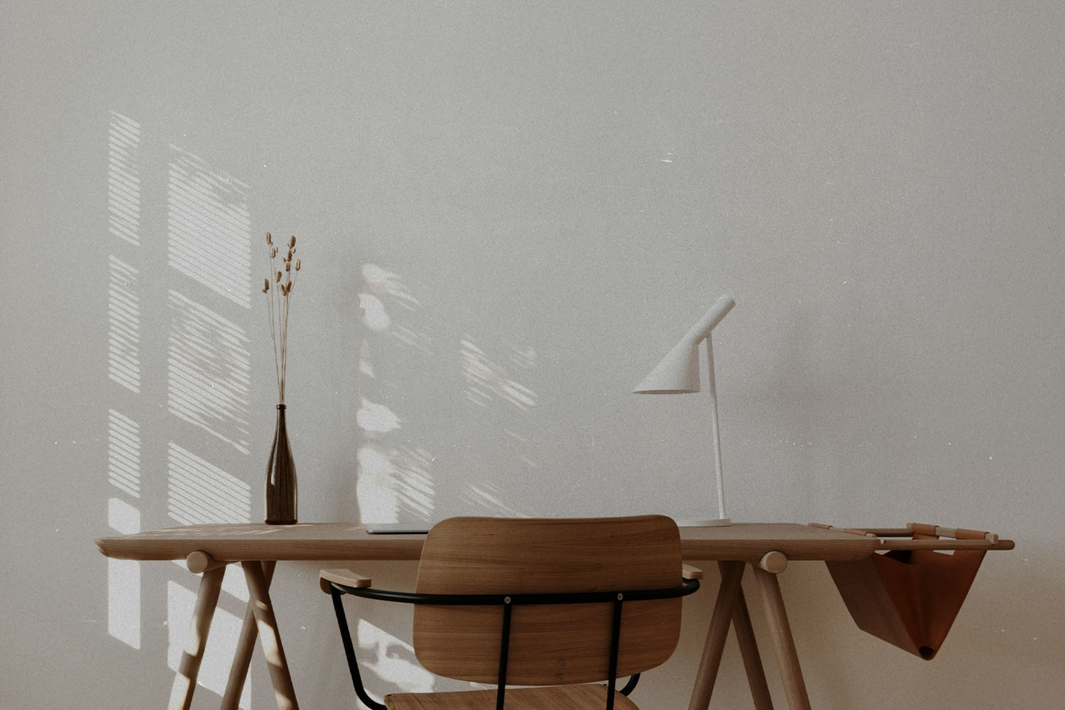 andinavian-style workspace featuring a wooden desk, simple chair, white lamp, and dried botanicals with sunlight filtering through a nearby window