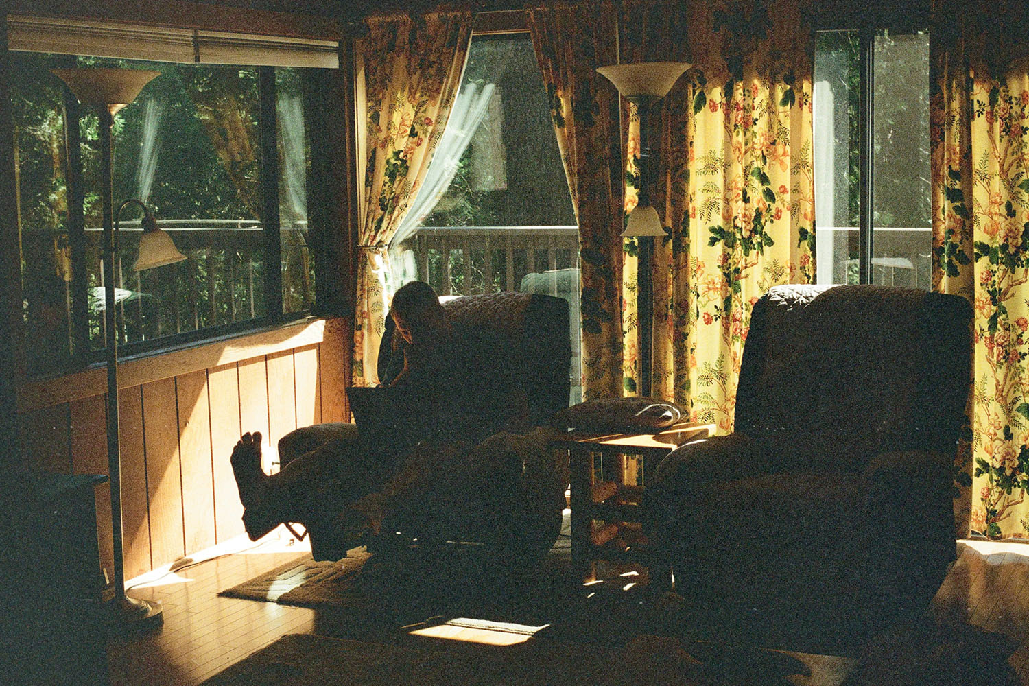 Cozy living room with patterned curtains and large windows, where someone sits in a recliner next to soft natural light