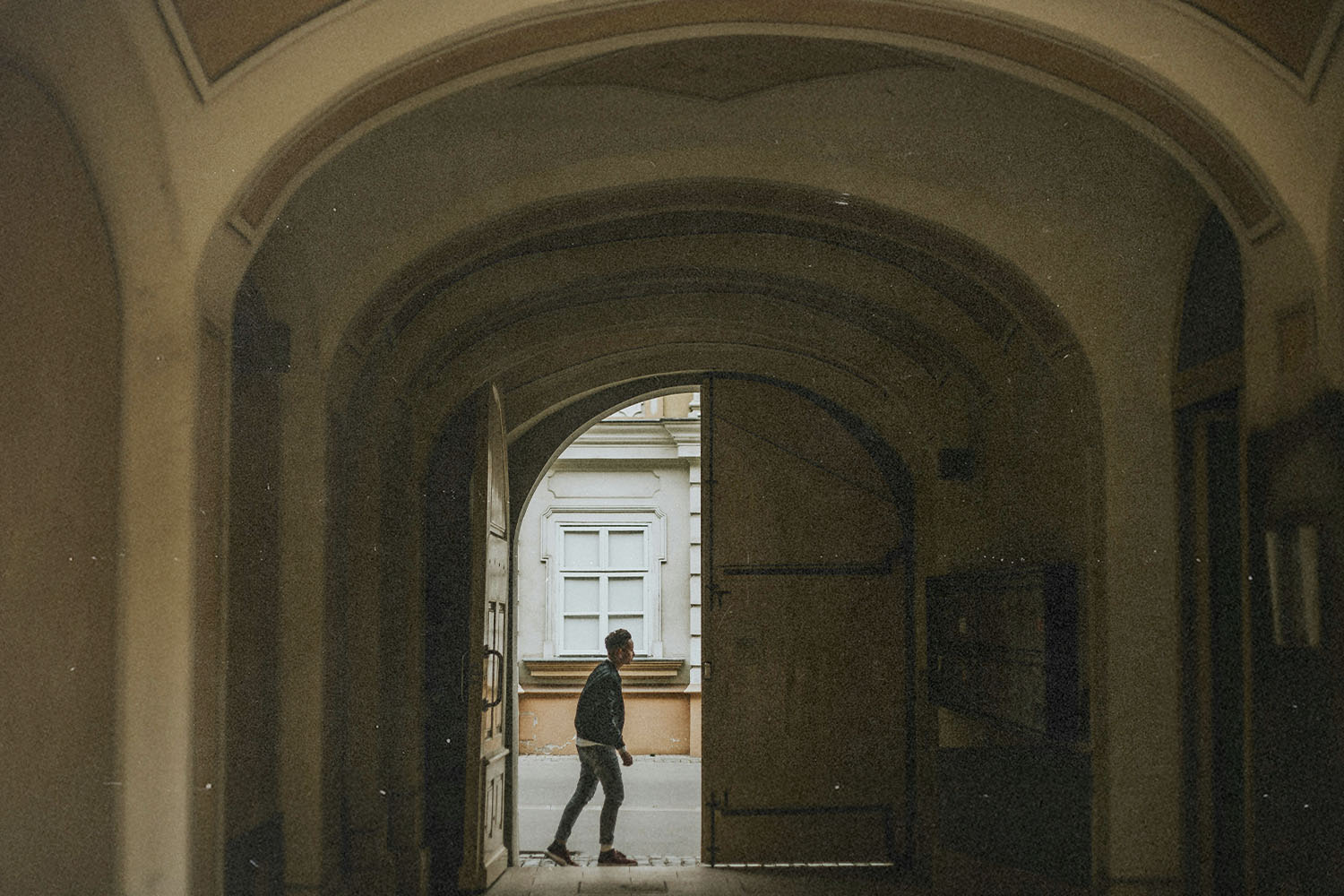 A person walks through a large arched doorway into a quiet courtyard, framed by the tall curved entryway