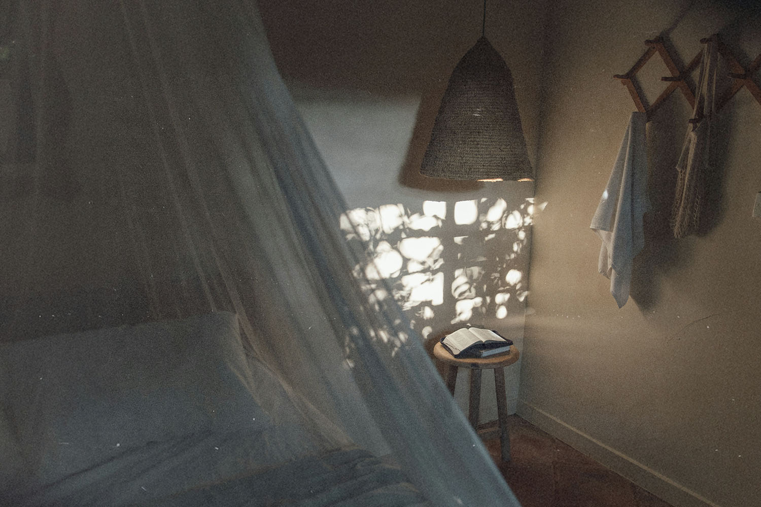 Soft morning light filters through a window into a cozy bedroom, illuminating an open book on a small wooden stool