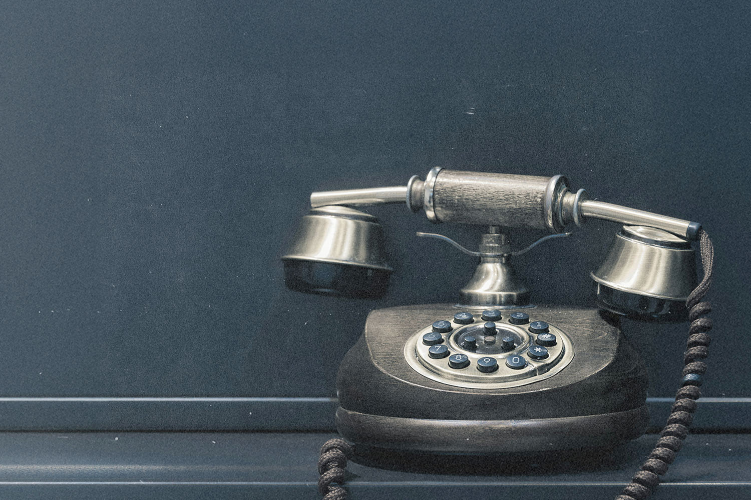 A vintage rotary telephone with a brass and wood finish sits against a dark matte background
