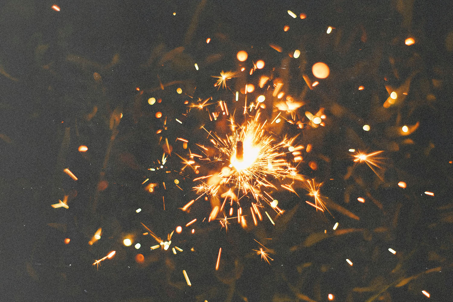 A single sparkler glows brightly in the dark, sending out golden sparks in all directions