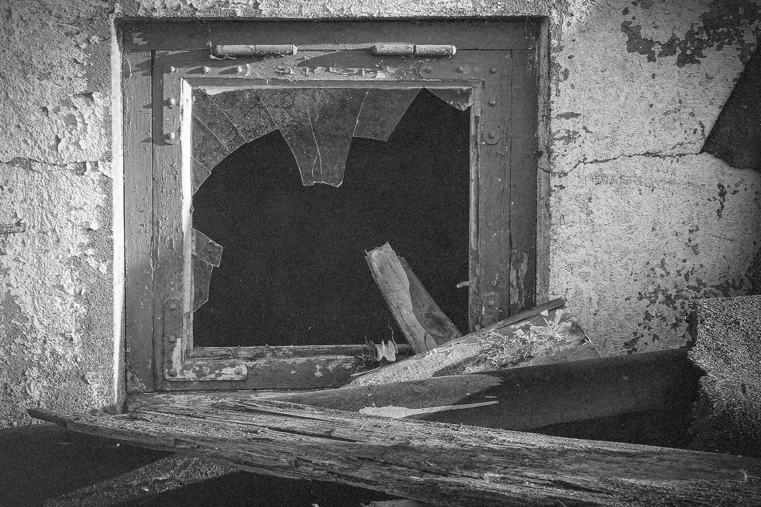A broken window with shattered glass sits in a weathered concrete wall surrounded by debris