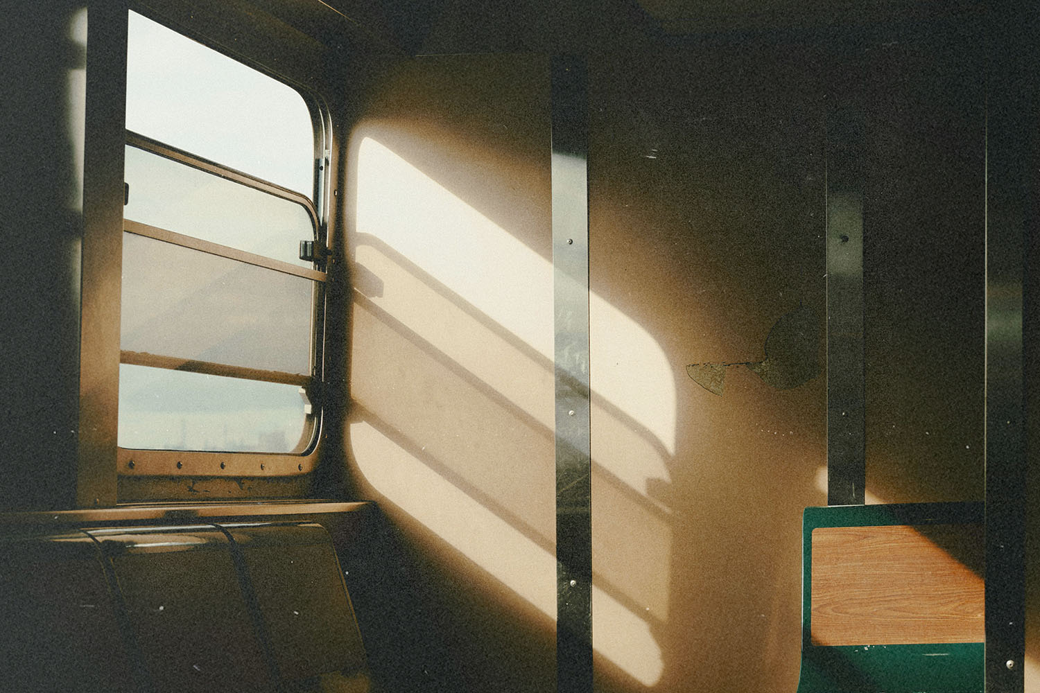 Warm sunlight streams through the window of an old train car, casting long, soft shadows across the beige interior walls and empty seats
