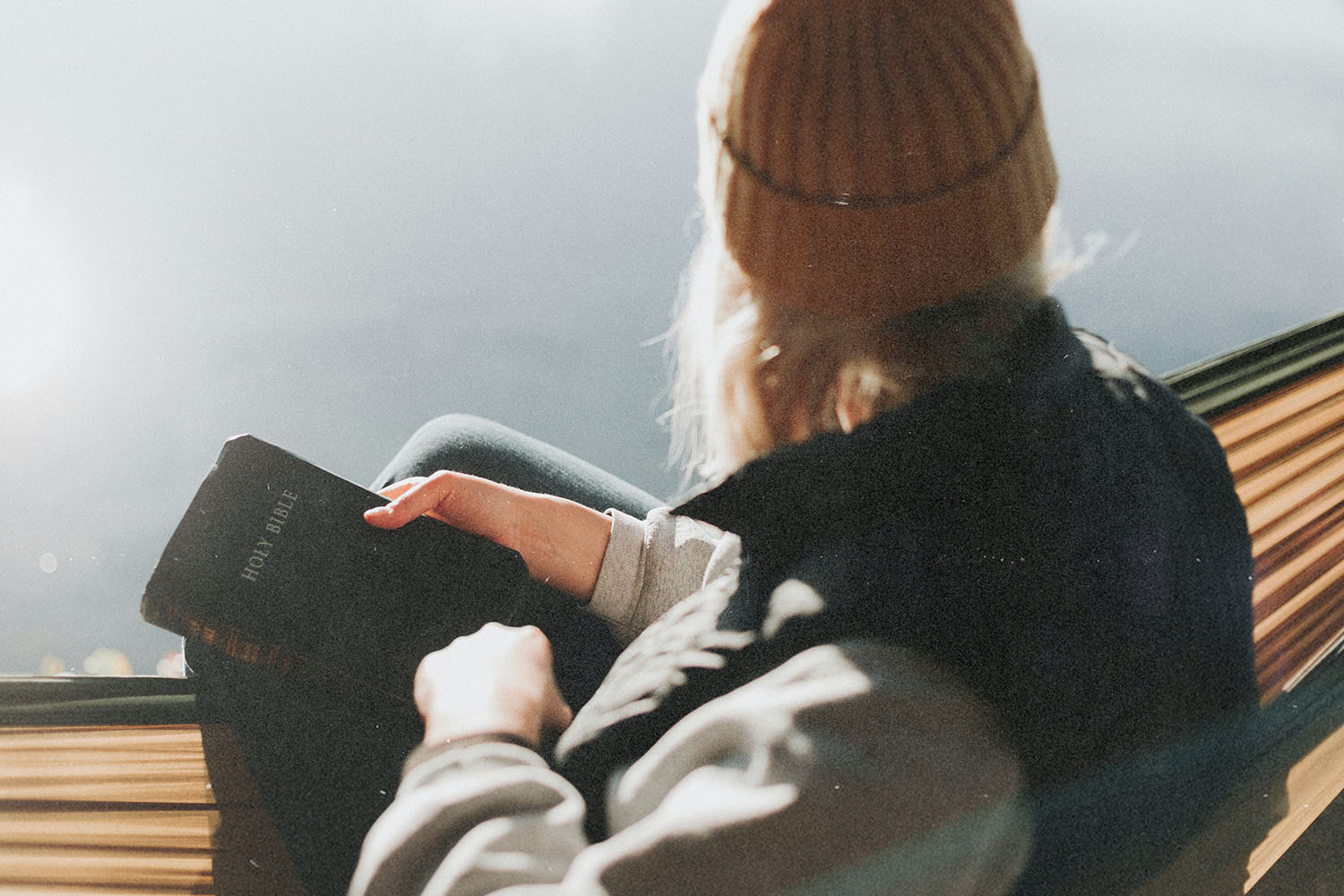 A person reclines in a hammock outdoors, holding a closed Bible while sunlight illuminates the scene