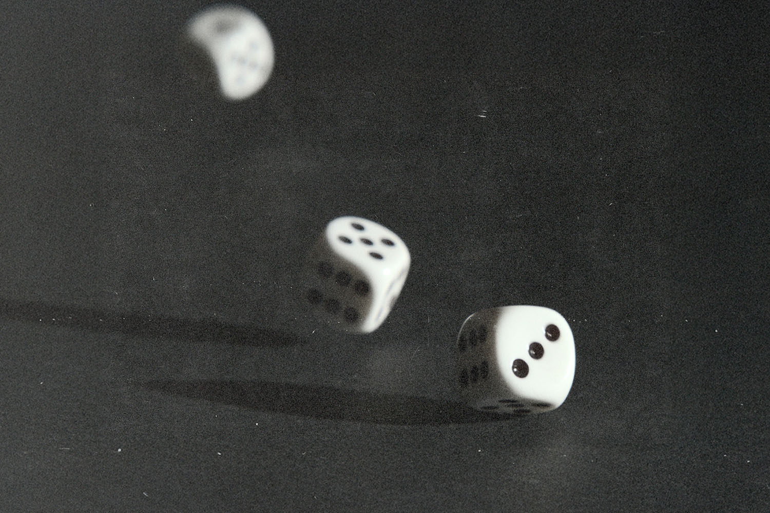 Three white dice captured midair and on a dark surface, frozen in motion as they tumble during a roll