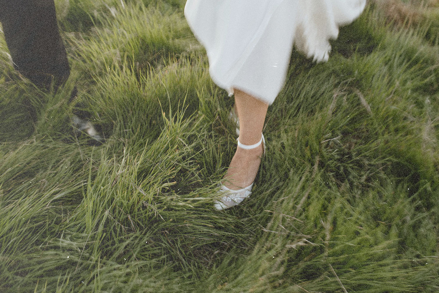 Feet stepping through tall green grass, with fabric moving gently around the legs