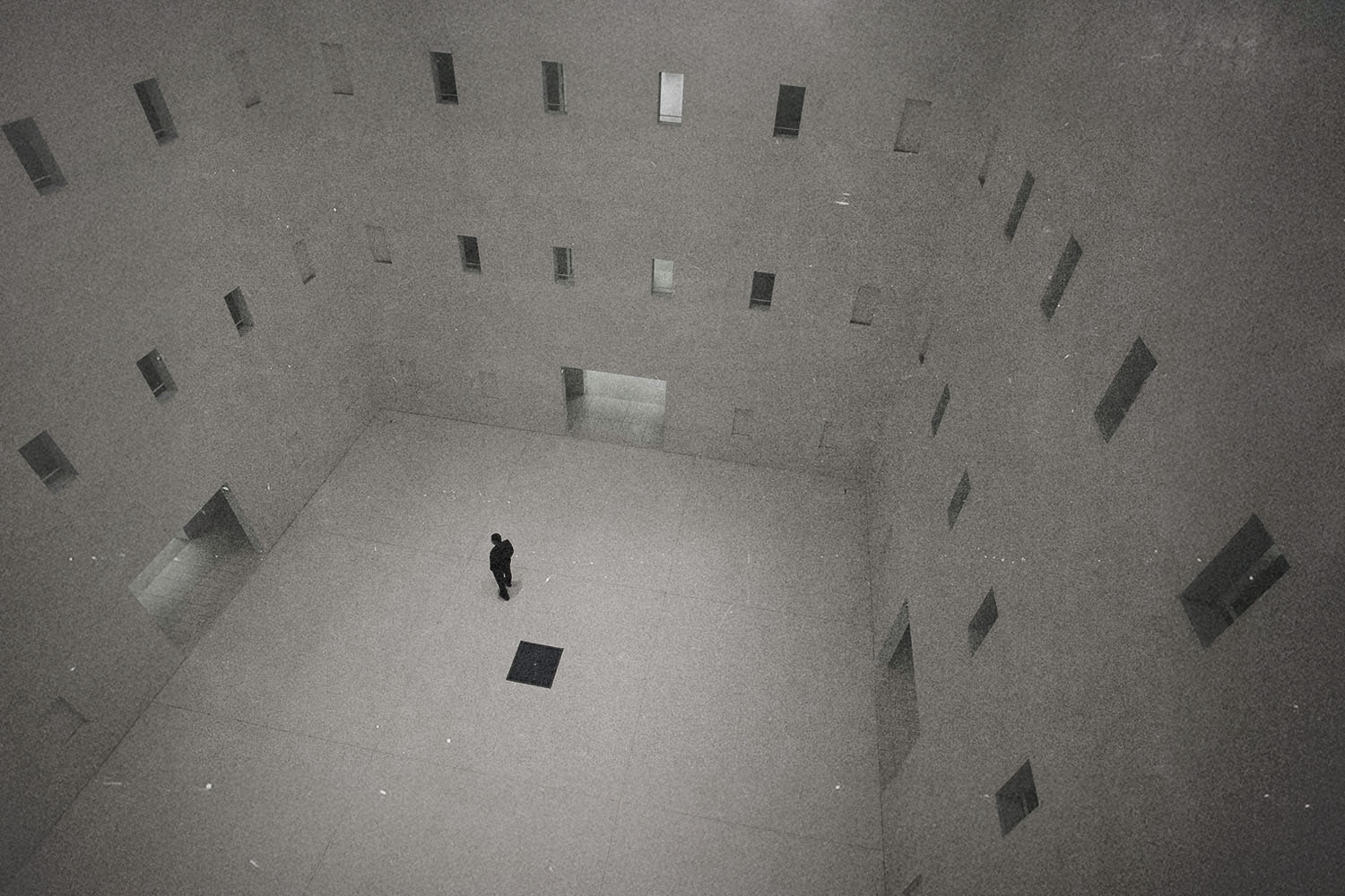 A solitary person standing in the center of a large, minimalist concrete interior with tall walls and narrow windows