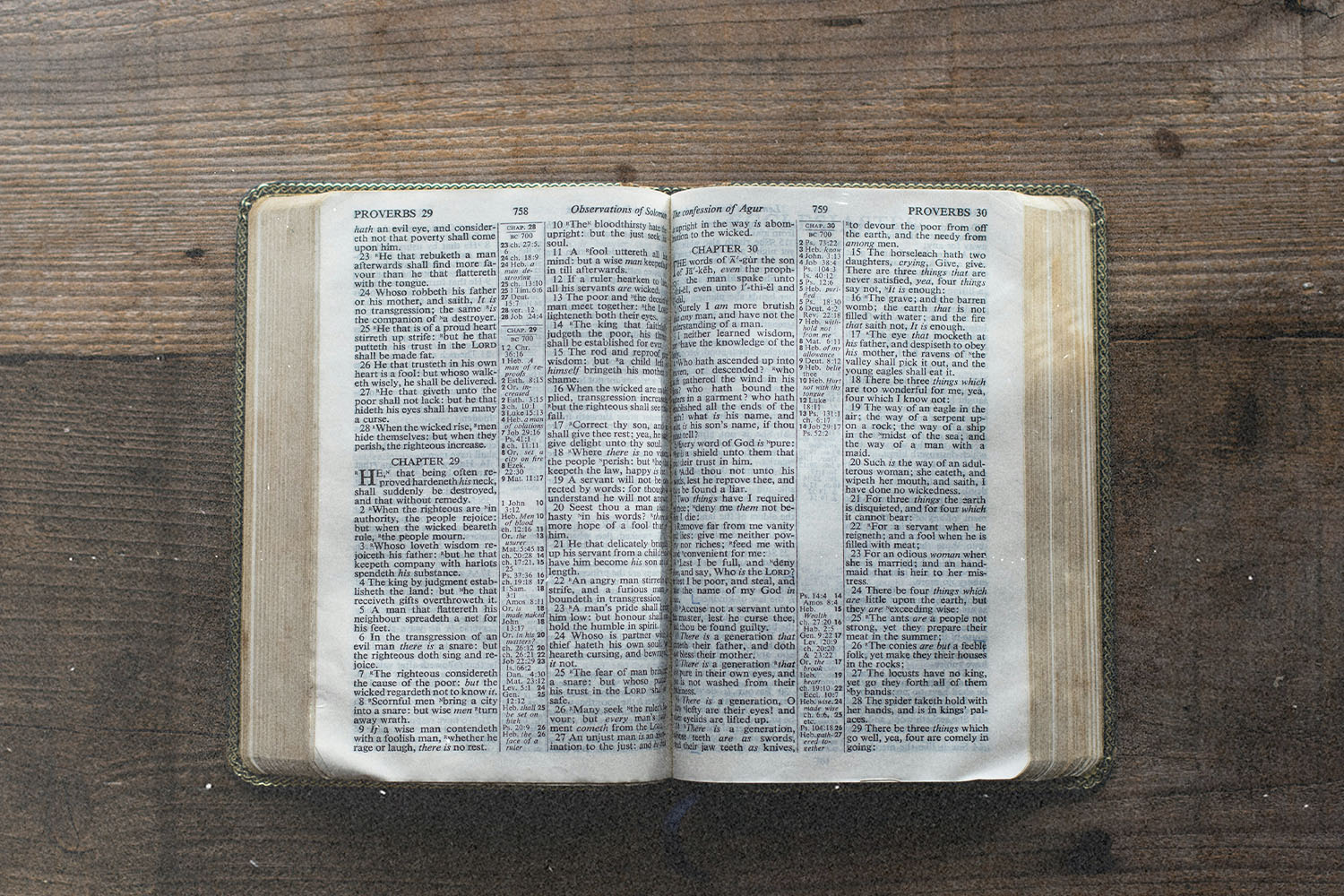 An open Bible lying flat on a wooden surface, viewed from above with text clearly visible on both pages