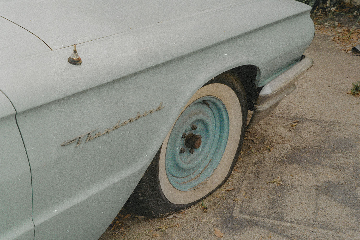 Close-up of a vintage car’s rear wheel and fender parked along a concrete curb
