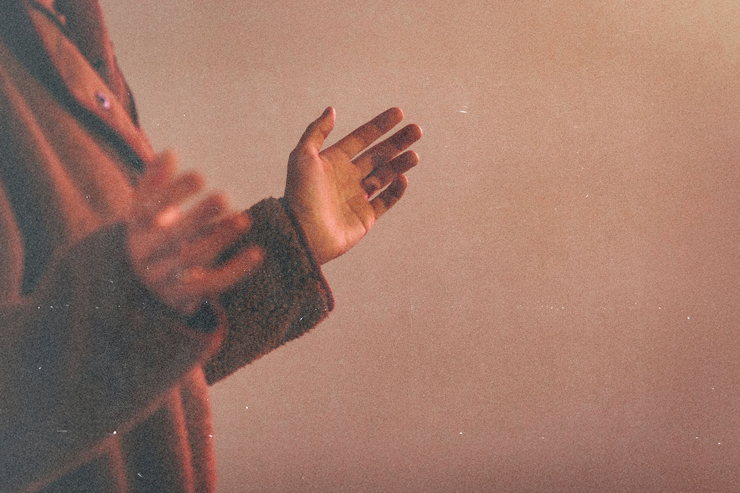 Hands raised slightly upward against a warm-toned background, suggesting prayer