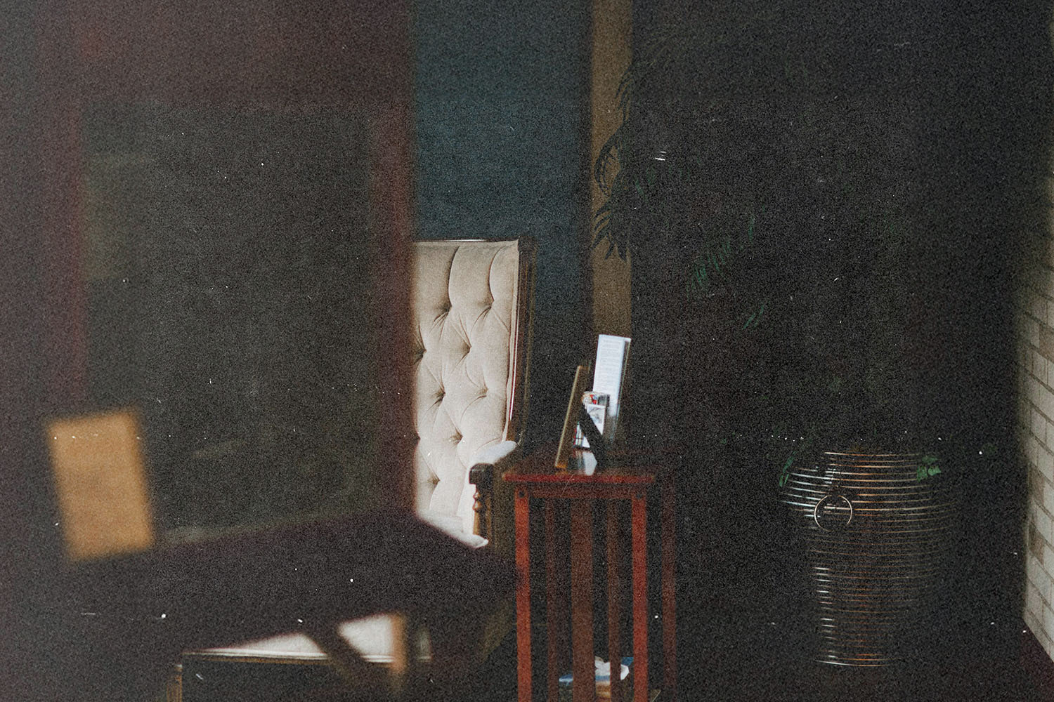 A softly lit interior room with an upholstered chair, a small side table, and a tall plant creating a calm atmosphere
