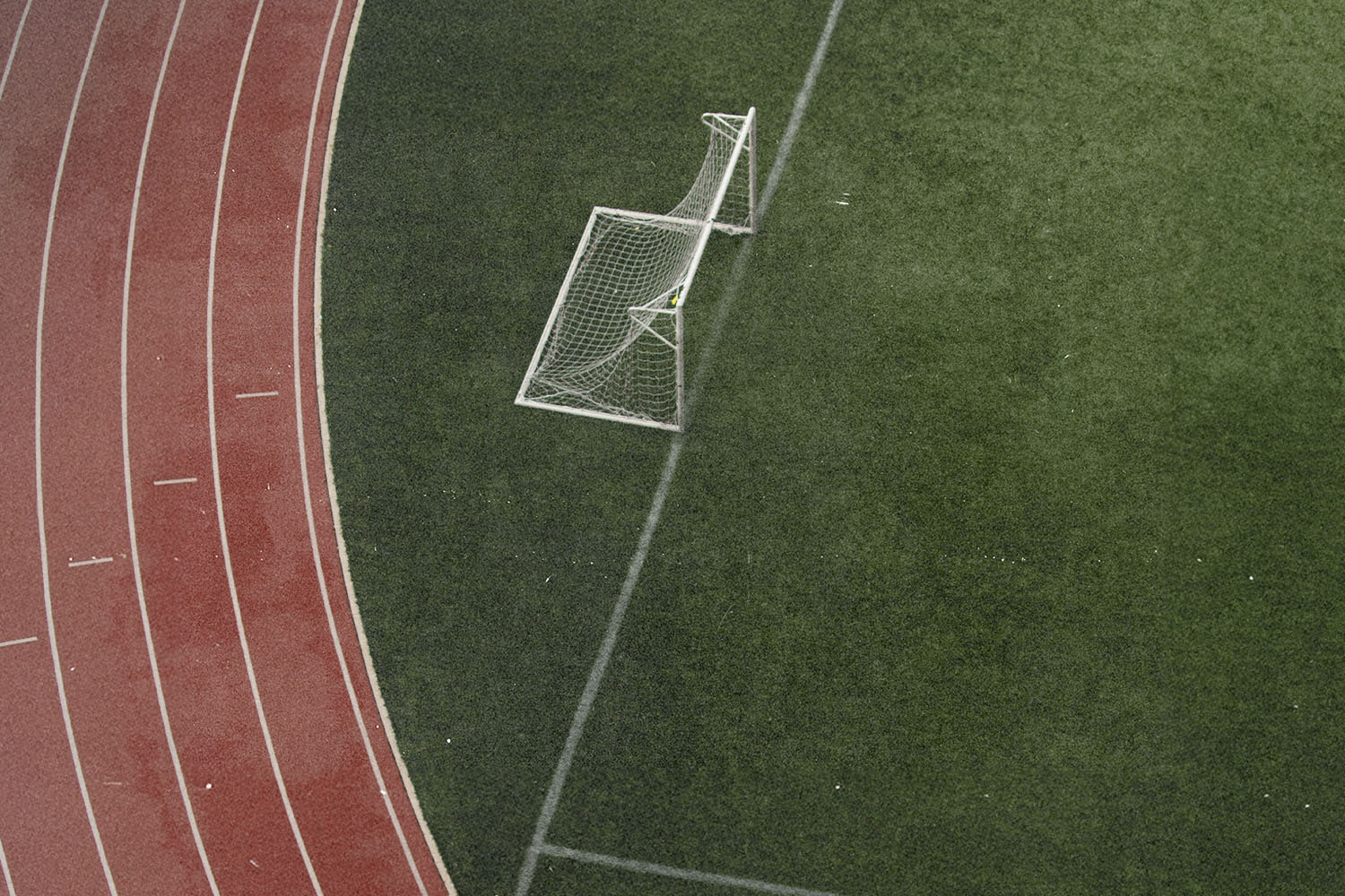 An aerial view of a soccer goal on a green field beside a red running track