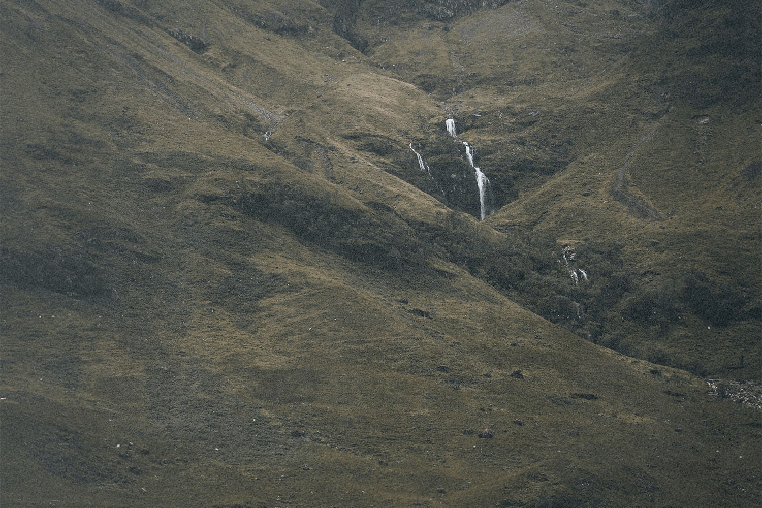 A wide view of rolling hills with a narrow waterfall cascading down the center of the landscape