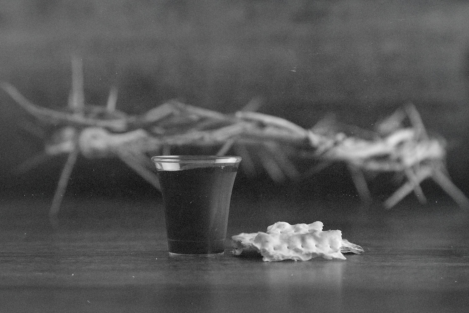 A small cup and a piece of bread placed on a table, with a crown of thorns visible in the background