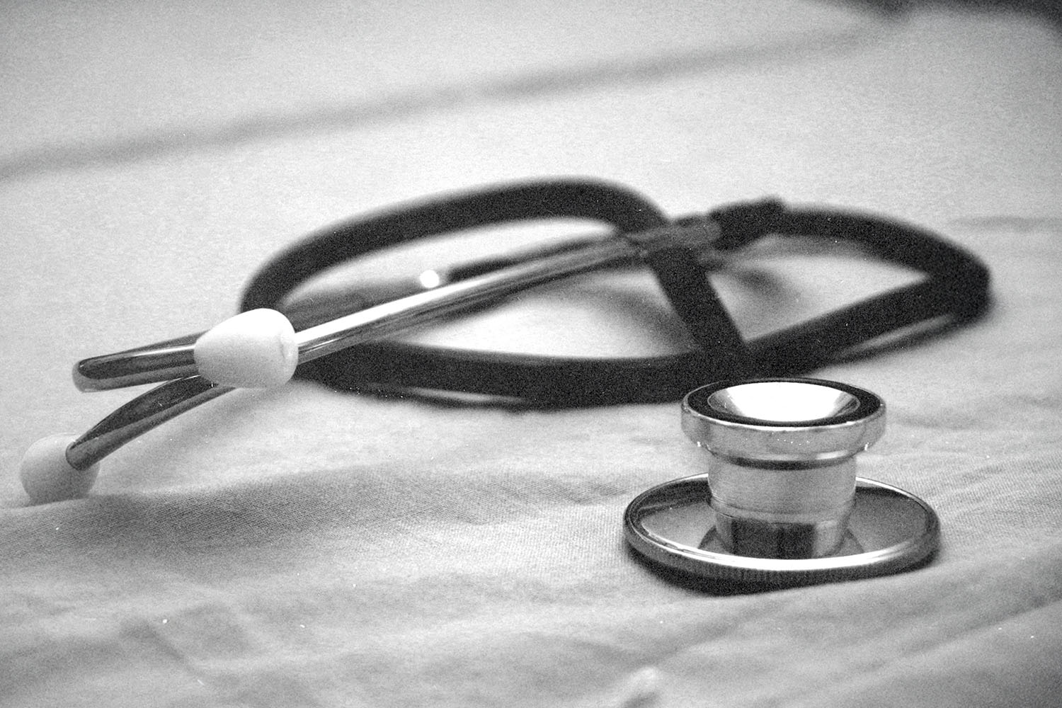 Stethoscope resting on a fabric surface in a softly lit black‑and‑white setting