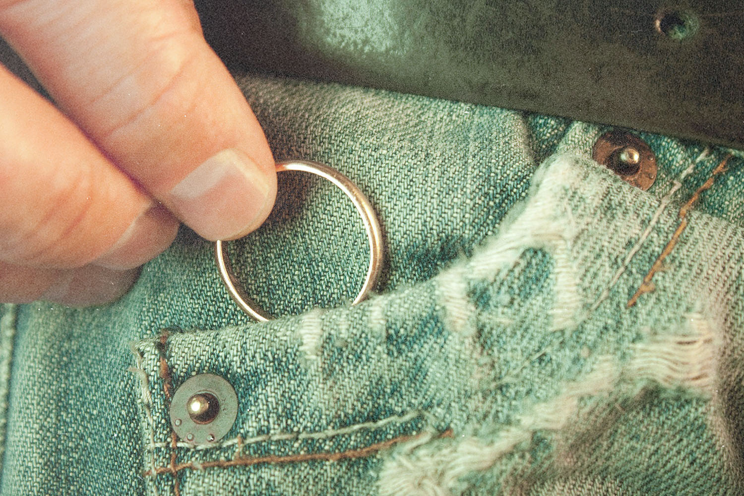 Hand placing a simple metal ring into the small front pocket of worn denim jeans