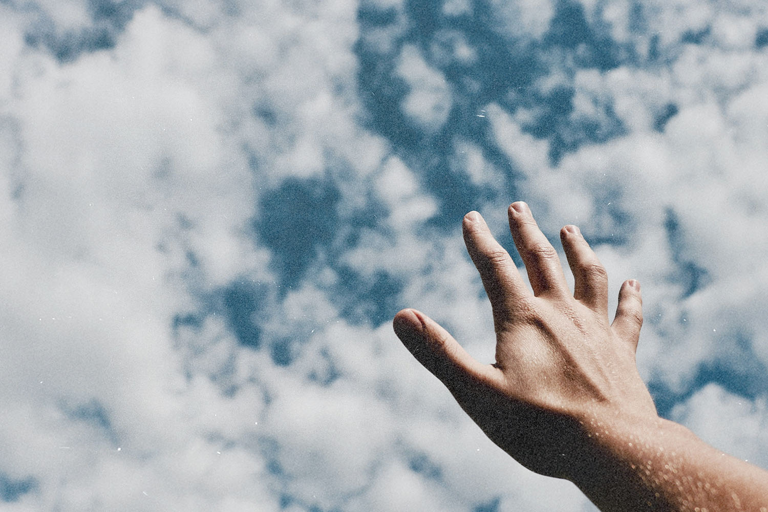 Hand extended upward toward a sky filled with scattered white clouds