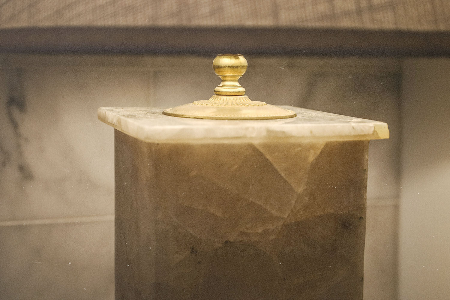 Marble column with an ornate gold finial on top in soft indoor lighting