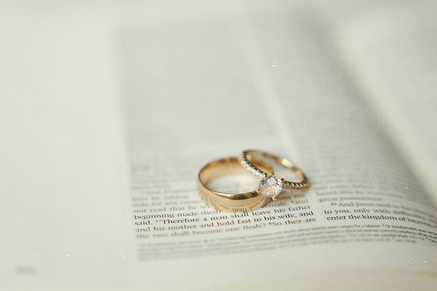 Gold wedding rings resting on an open Bible with the text softly blurred around them