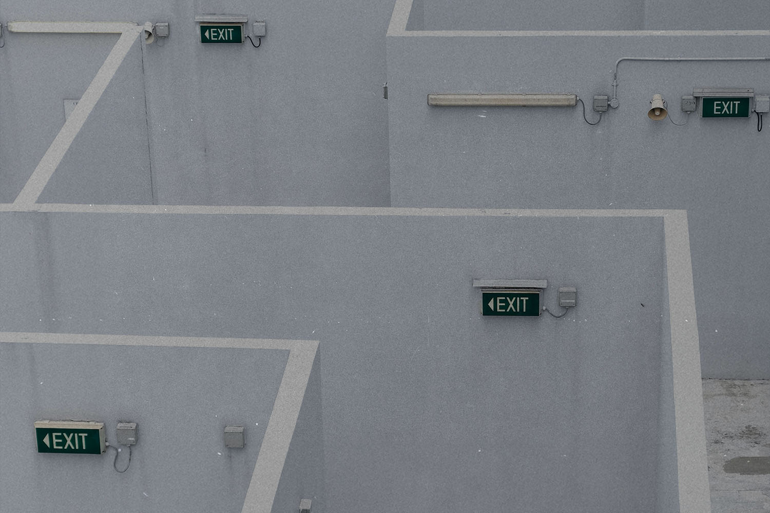 Series of concrete walls forming a maze-like structure with green illuminated exit signs mounted throughout