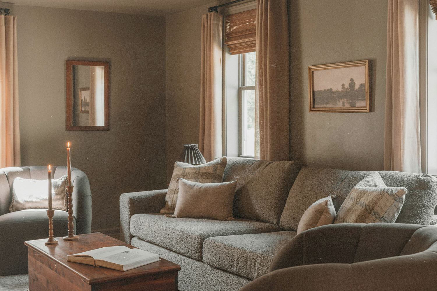 Warm living room with sofas, candles, framed wall art, and a wooden coffee table near softly lit windows